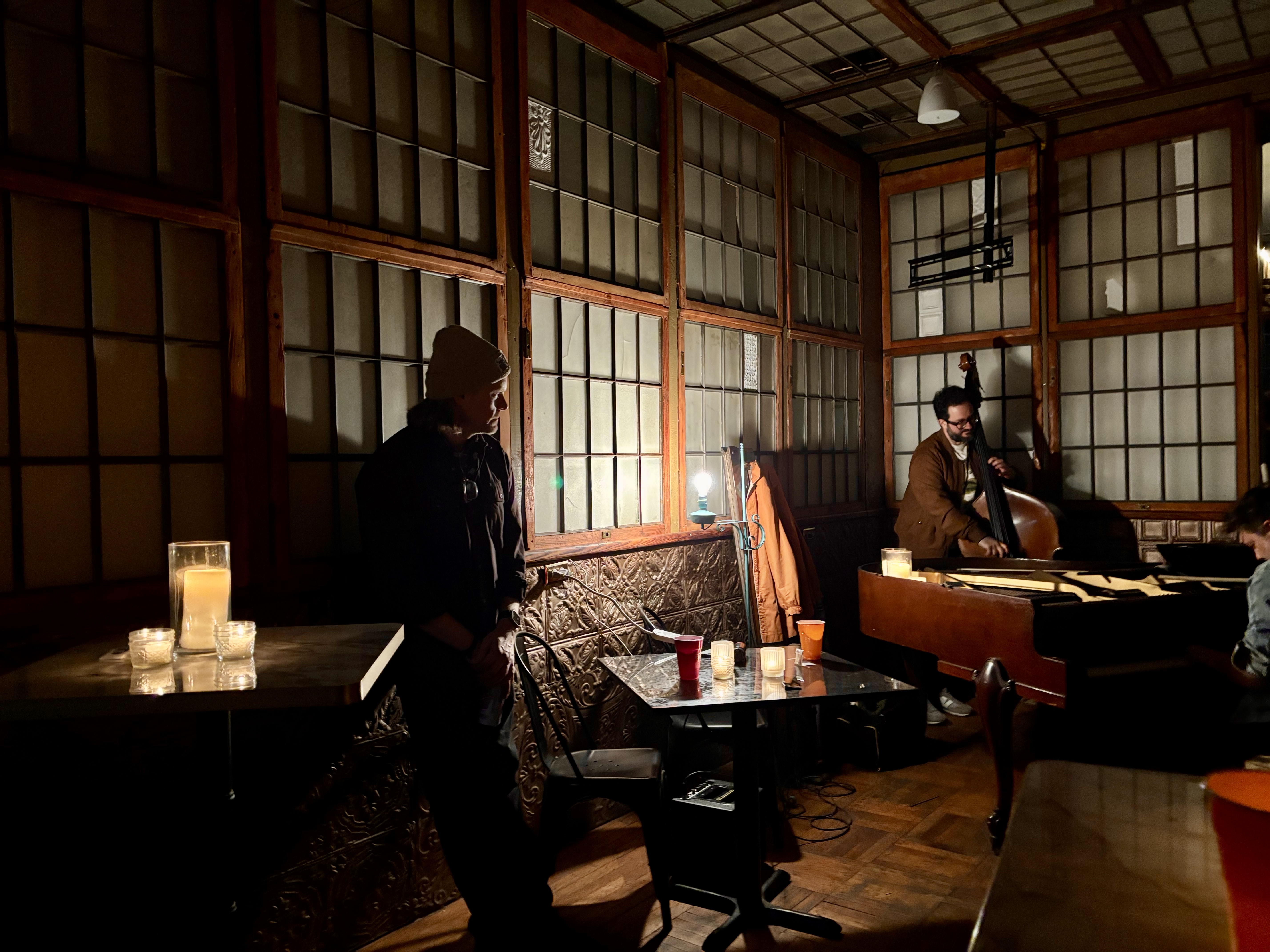 A bassist playing in the corner while the room glows with candlelight.