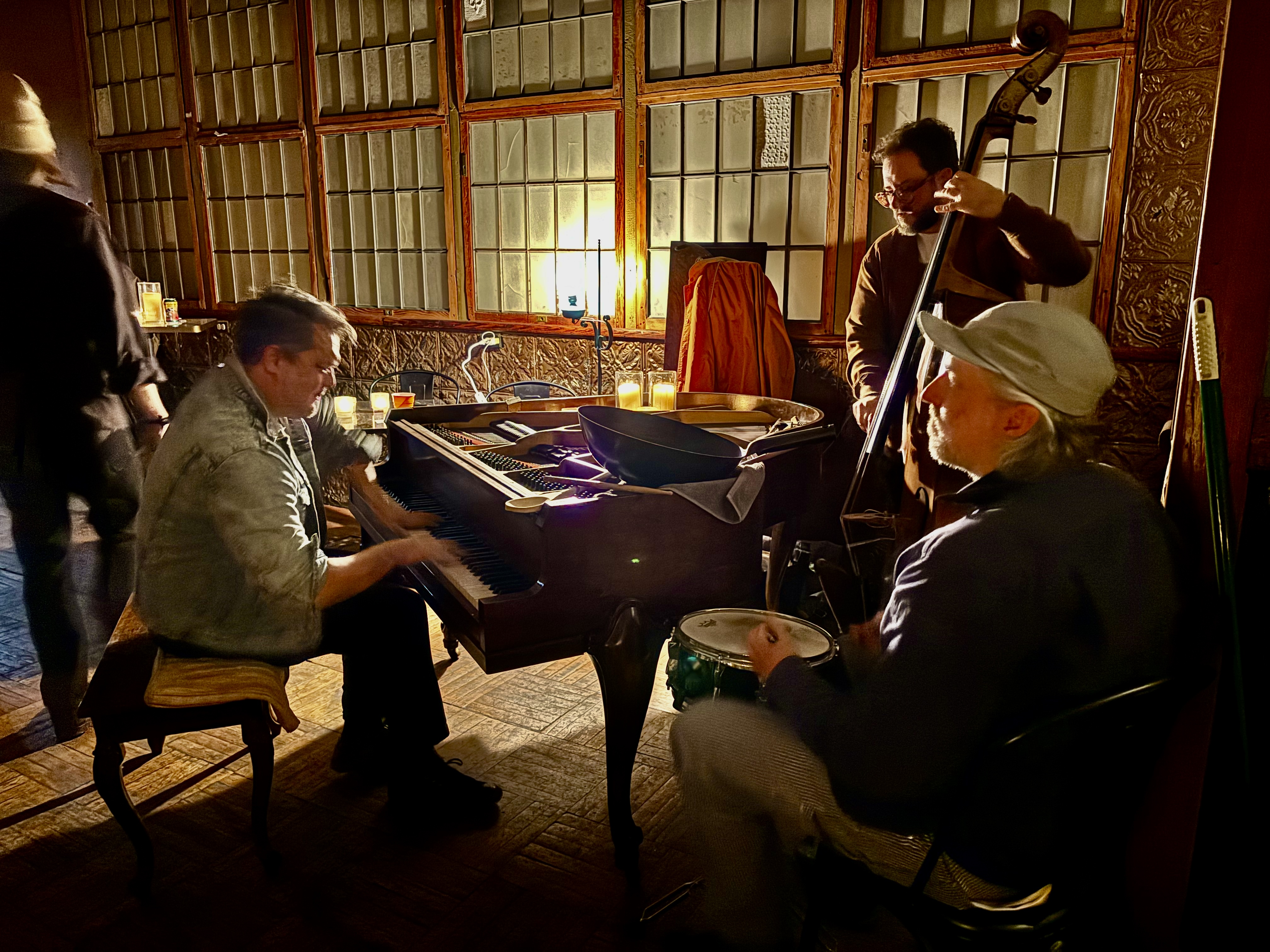A pianist, bassist, and drummer playing close together around the piano.